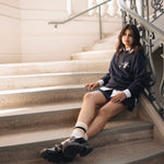 Woman posing leaning on stairs wearing grey crewneck sweater, skirt and mary jane shoes