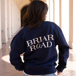 Woman facing backwards, wearing a navy blue long sleeved crewneck with Briar Road branding