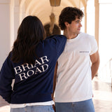 Couple posing. Woman wearing a navy blue crewneck sweater with Briar Road branding. Man wearing a white short sleeved crewneck and looking sideways.