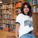 Woman leaning on a table wearing a styled white crewneck with jeans and a blue polo