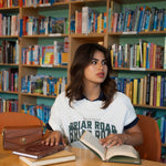 Woman sitting with books wearing white graphic crewneck