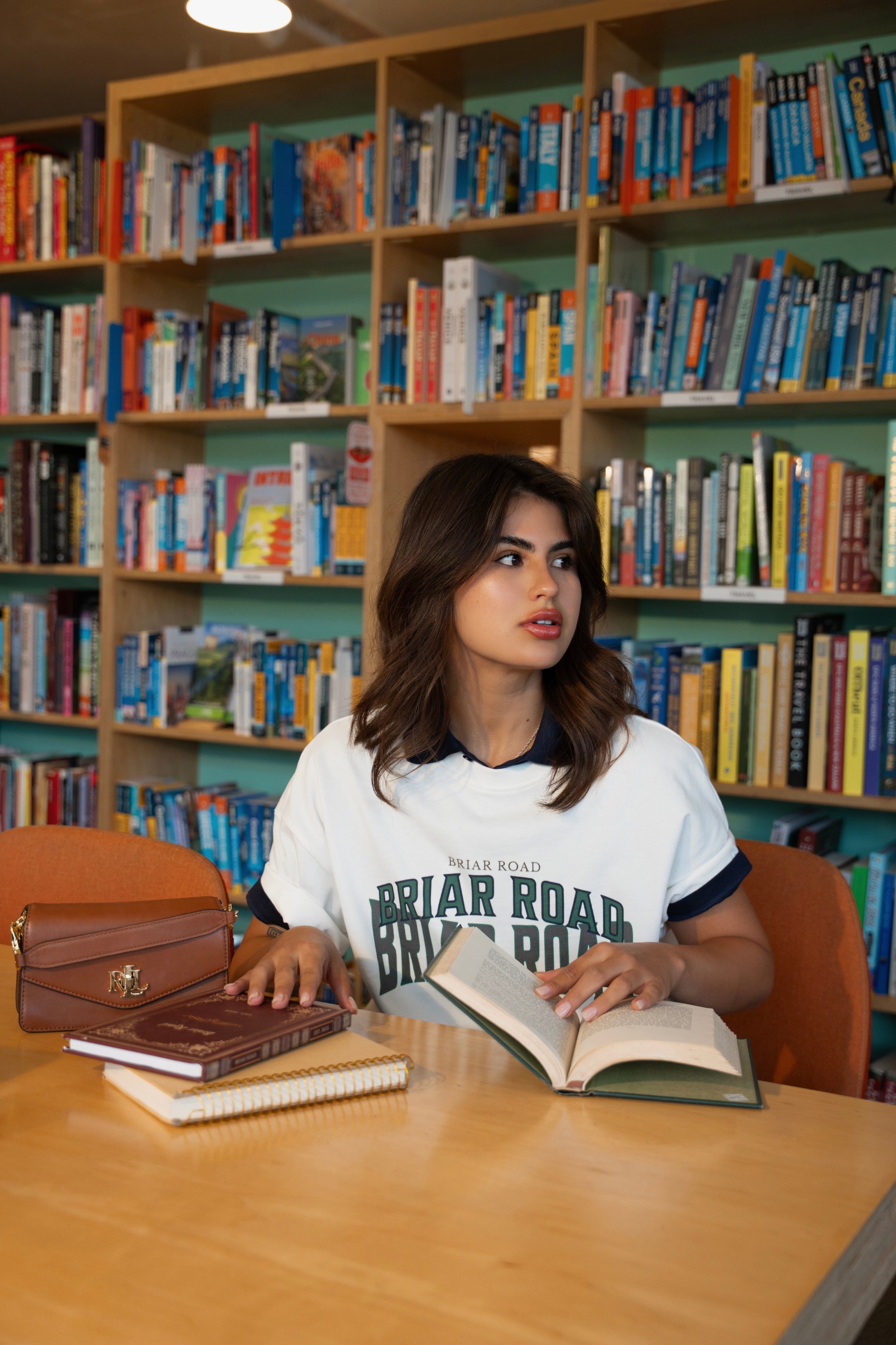 Woman sitting with books wearing white graphic crewneck